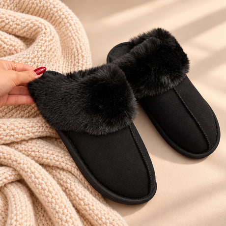 Hand holding a black suede look slipper with a fluffy black fur collar