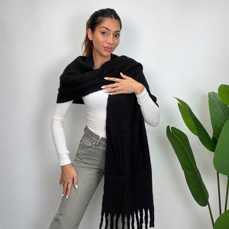 Woman wrapping a black brushed blanket scarf over her shoulder with long twisted tassels