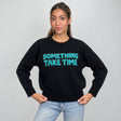 Black knit sweater with fuzzy teal slogan lettering across the chest, hands on hips