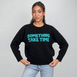 Black knit sweater with fuzzy teal slogan lettering across the chest, hands on hips