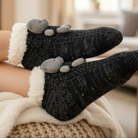 Black teddy socks worn by a person, sitting on a couch.