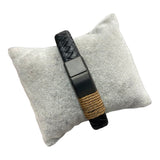 Black braided leather bracelet with steel clasp and tan cord wrap on a display cushion