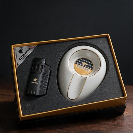 Matte black vented torch lighter beside a white ceramic cigar ashtray with gold rim in a gift box