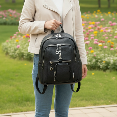 Person holding a black urban backpack in a park with flowers in the background