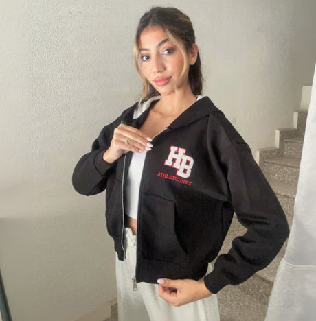 Black varsity patch zip hoodie worn open over a white top with grey joggers