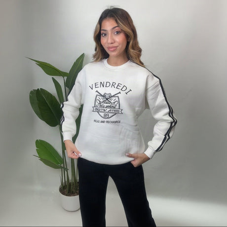 White varsity print sweatshirt with black sleeve stripes and black wide leg pants, hands on hips
