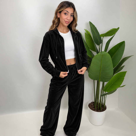 Woman in a black velour cropped zip hoodie worn open over a white crop top with matching wide leg pants