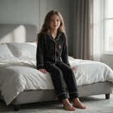 Girl sitting on a bed in black velvet pyjamas showing the embroidered chest pocket