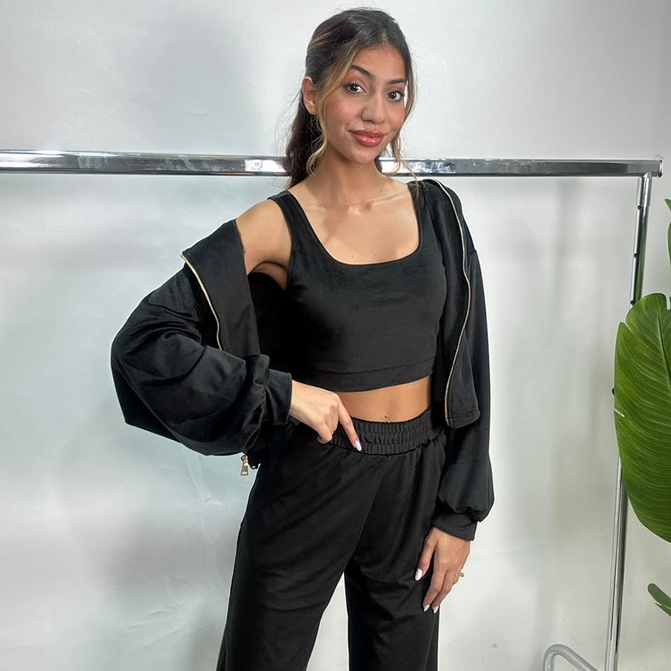 Black velvet jacket held off one shoulder showing the scoop neck crop top and wide leg pants