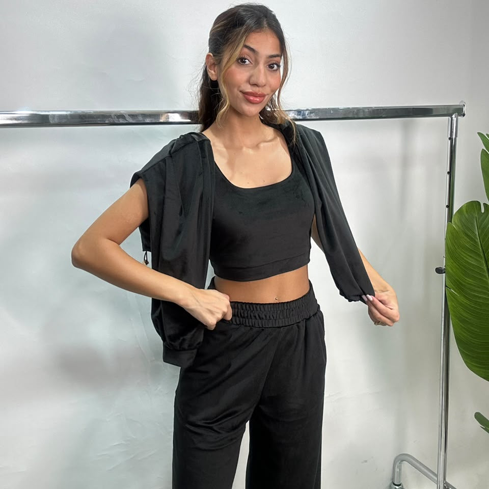 Woman in a black velvet zip jacket slipped off the shoulders over a matching crop top and pants