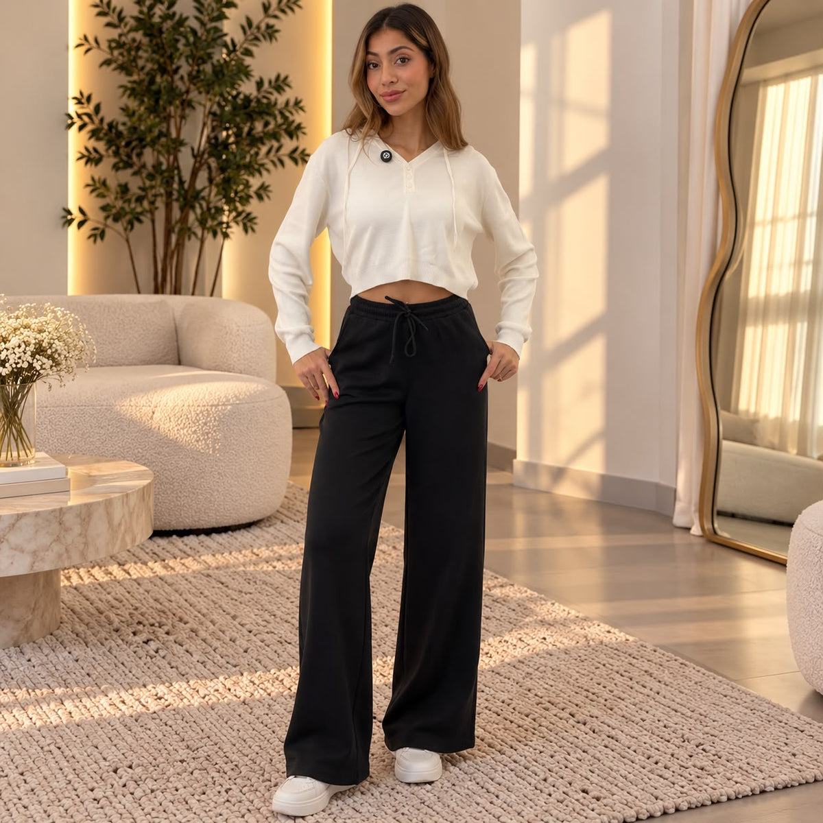 Woman in black wide leg sweatpants and a cream cropped top standing in a bright living room