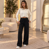 Woman in black wide leg sweatpants and a cream cropped top standing in a bright living room