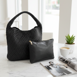 Black woven handbag and clutch on a marble surface with a cup of coffee and newspaper in the background