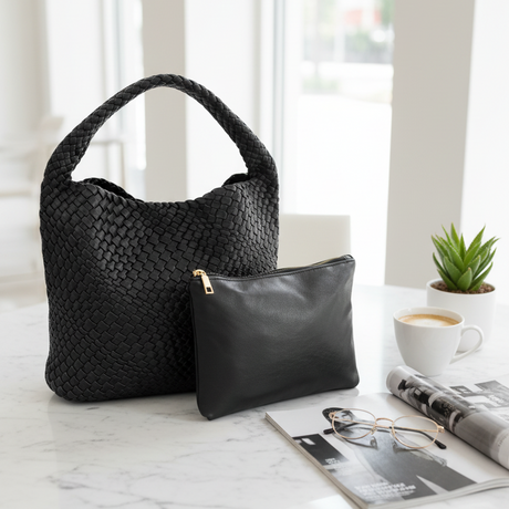 Black woven handbag and clutch on a marble surface with a cup of coffee and newspaper in the background