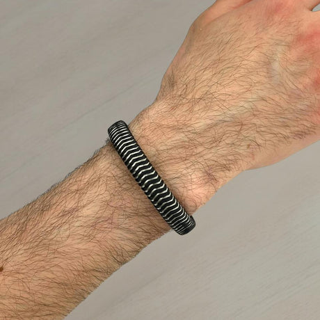 Hand wearing a black and silver striped bracelet on a neutral background