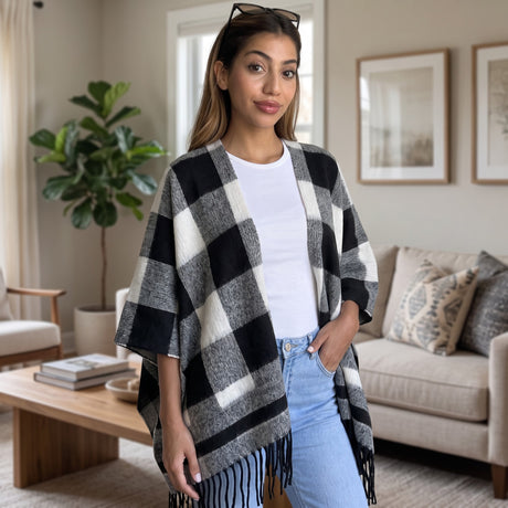 Woman wearing an open front black and white check poncho with fringed hem over jeans