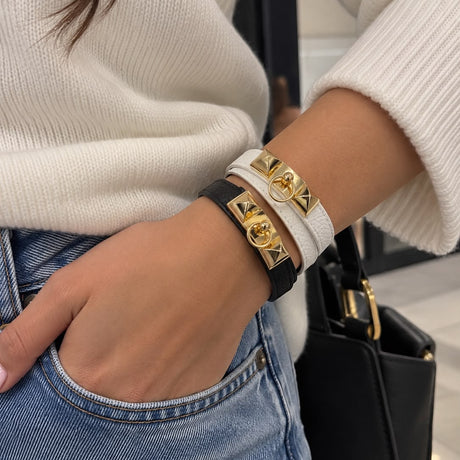 Woman wearing black and white wrap bracelets with gold pyramid studs, stacked on her wrist with a cream sweater