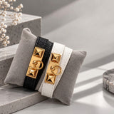 Black and White pyramid stud wrap bracelets with gold ring clasps displayed on a grey velvet cushion