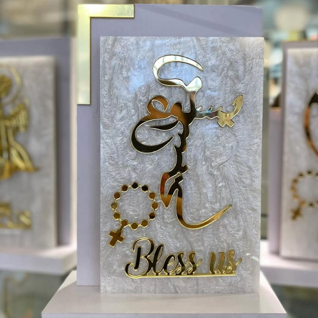 Large gold Arabic calligraphy on a marbled panel with Bless us scripted beneath