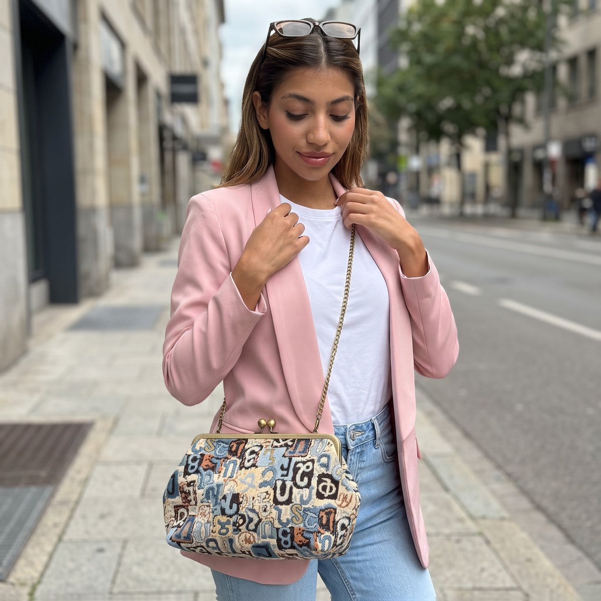 Woman in a pink blazer with a blue Armenian letter tapestry bag worn over the shoulder