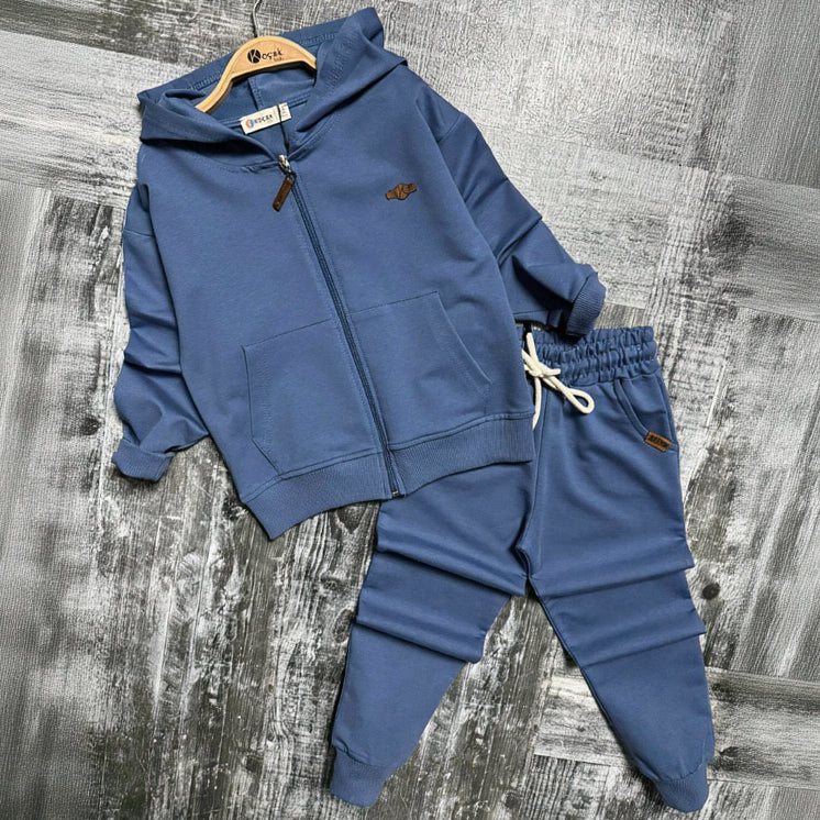 Blue zip up hooded jacket with front pockets and matching cuffed joggers on a grey backdrop