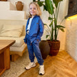 Young boy wearing a blue zip up hooded tracksuit with cuffed joggers and beige sneakers