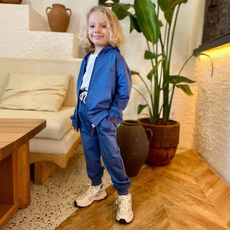 Young boy wearing a blue zip up hooded tracksuit with cuffed joggers and beige sneakers