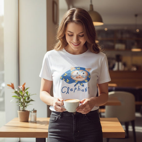 Woman holding a cup of coffee in a cafe wearing a t-shirt with a cat design and 'Clephant' text