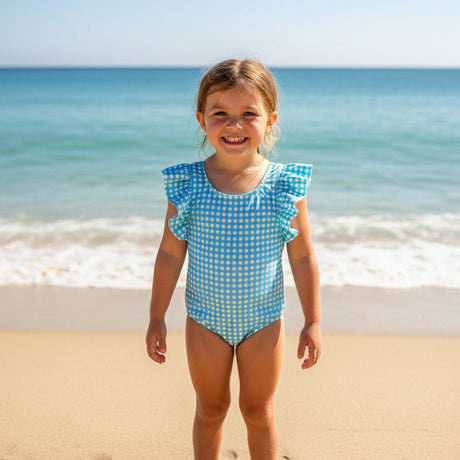 Girl wearing a blue checkered onepiece swimsuit with ruffled cap sleeves on the beach