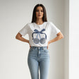 Woman wearing a white tshirt with a blue cherry design and light blue jeans on a plain background