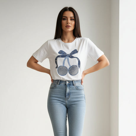 Woman wearing a white tshirt with a blue cherry design and light blue jeans on a plain background