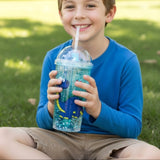 Boy on the grass drinking from an aqua dinosaur glitter cup