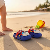 Blue puppy clogs resting on sand beside a toy bucket at sunset