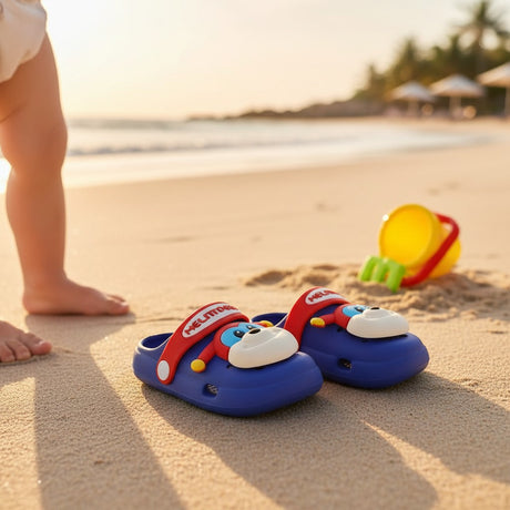 Blue puppy clogs resting on sand beside a toy bucket at sunset