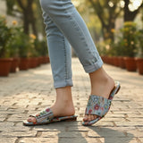 Pale blue floral tapestry slides worn with cuffed jeans on a park path