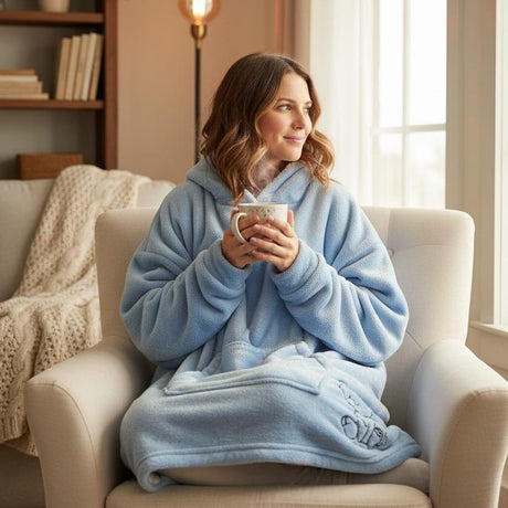 Woman in a cozy blue robe holding a mug, sitting on a couch in a warm living room.