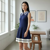 Woman wearing a blue dress with white trim in a room with large windows and a wooden table