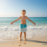 Child in blue lead design swim shorts standing on a beach with ocean waves