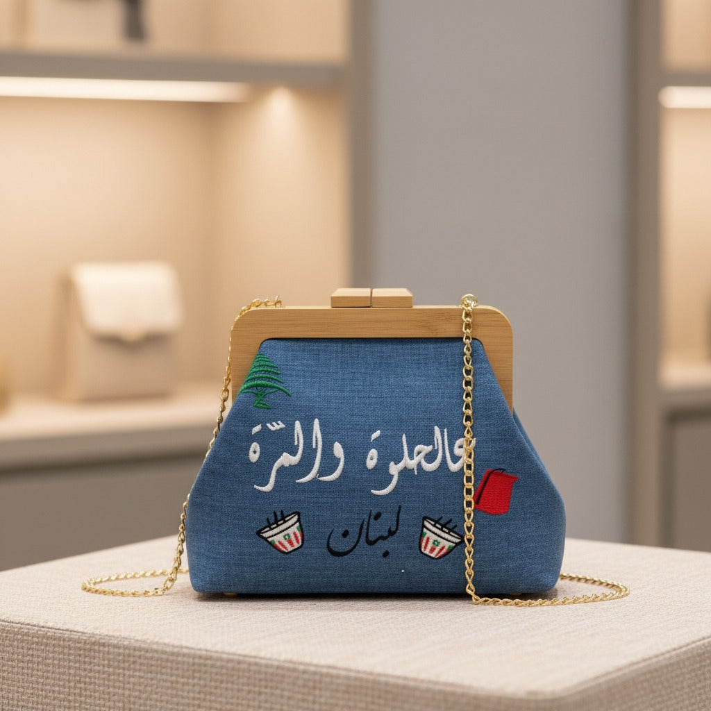 Blue heritage bag at an angle with white Arabic embroidery and a long gold chain