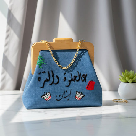 Blue woven frame bag with a wooden clasp, green cedar, black Arabic script and two coffee cups