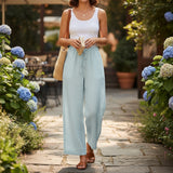 Woman in a white top and light blue pants standing in a garden with flowers and plants