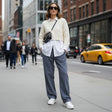 Woman in a cream sweater and blue linen pants walking on a city street