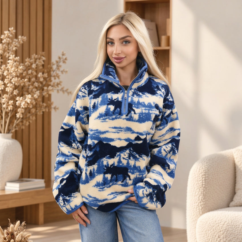 Woman in a cream and blue sherpa half zip pullover with navy moose, mountains and pine trees