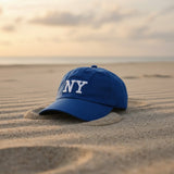 Royal blue embroidered cotton cap resting on rippled sand at dusk
