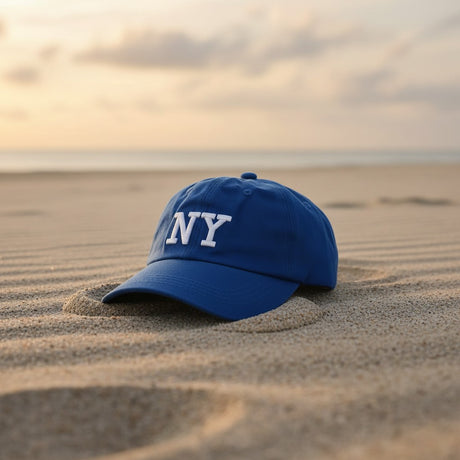 Royal blue embroidered cotton cap resting on rippled sand at dusk