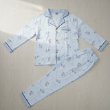 Light blue cartoon dinosaur print button front kids pyjama set laid flat on a wood floor