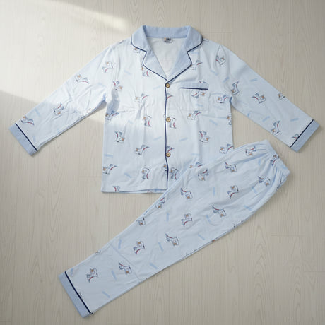 Light blue cartoon dinosaur print button front kids pyjama set laid flat on a wood floor