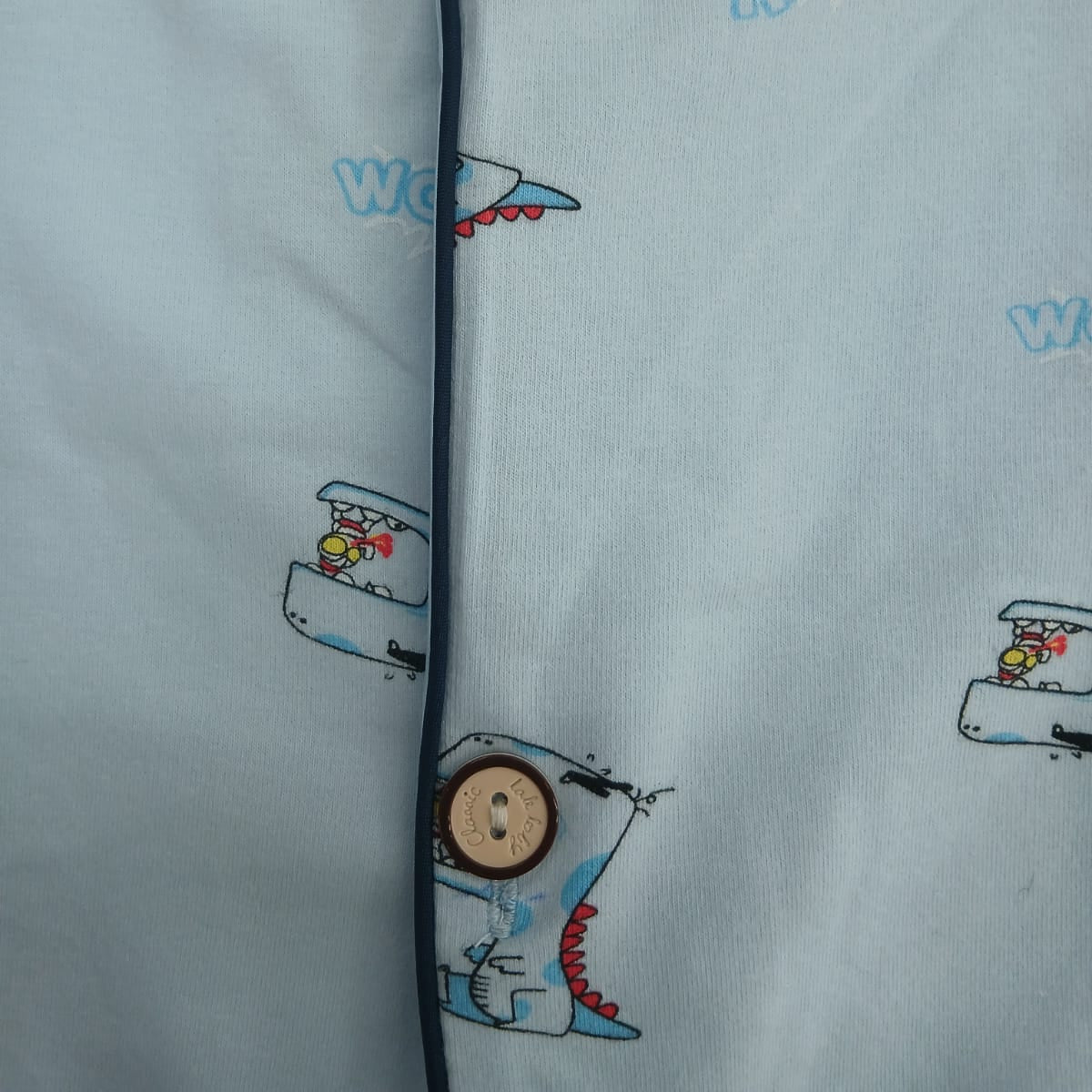 Button placket close up with navy piping and cartoon dinosaur print on light blue pyjama fabric