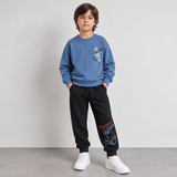 Boy in a blue skateboard sweatshirt and black printed joggers, front view