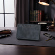 Blue leather wallet on a desk with a pen, keys, and a cup in the background.